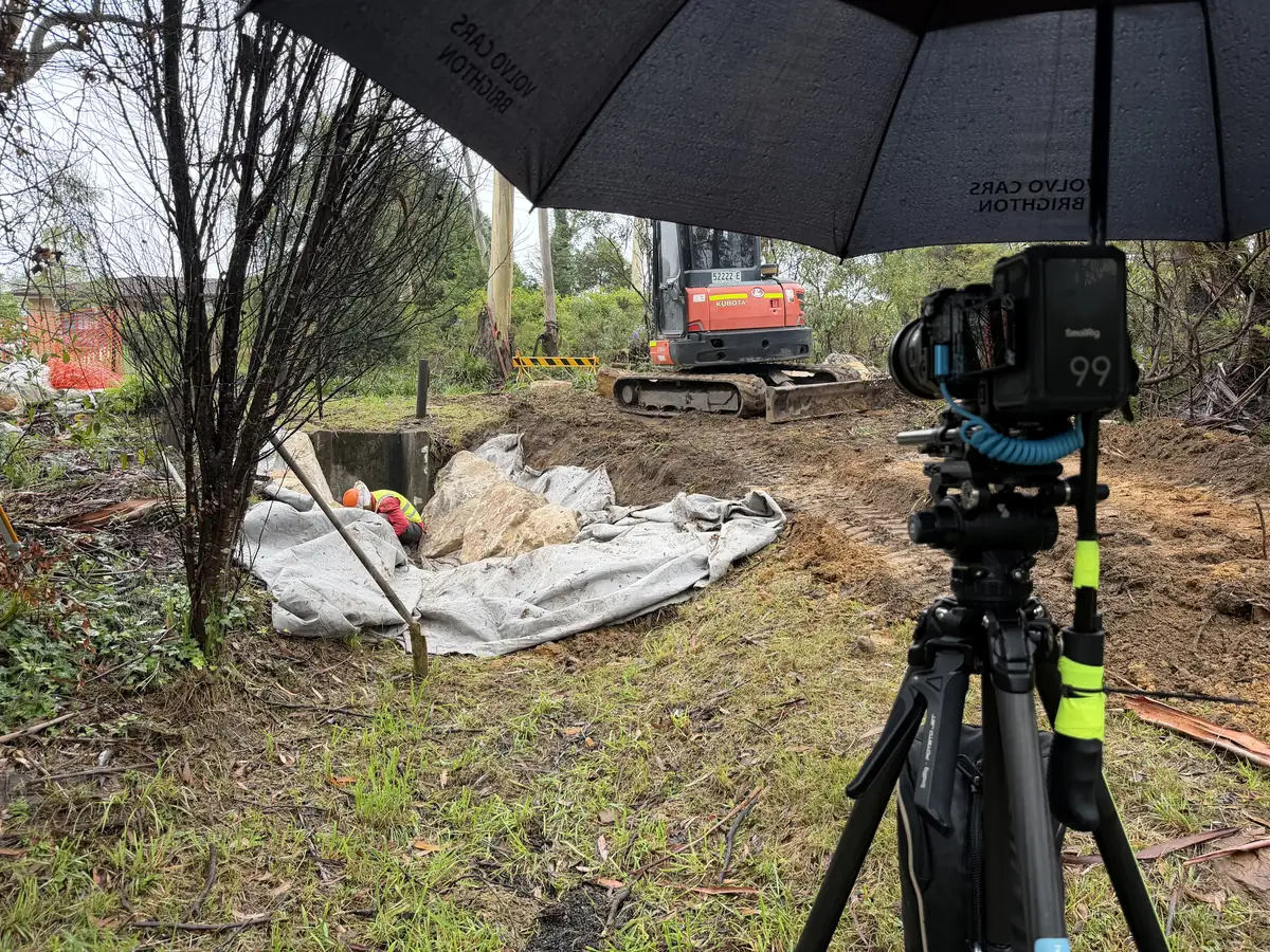 Cinema camera on a tripod under a rain umbrella at a construction site, filming a customer testimonial on location